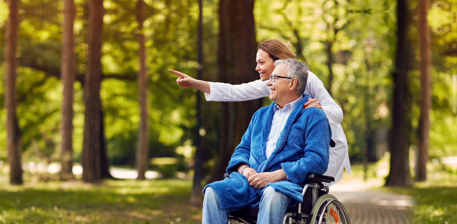 elder man on wheelchair together with his caregiver looking at distance