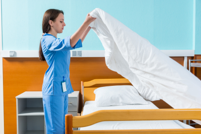 young nurse in blue uniform changing bed sheets